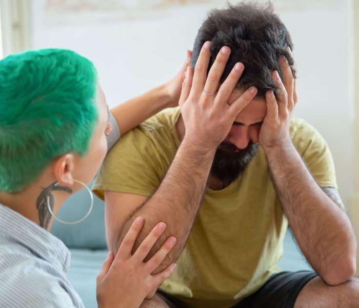 Person sitting with their head in their hands while another person offers comforting support during a difficult moment.