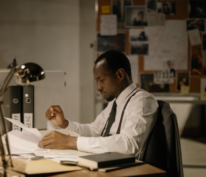 A professional sitting at his desk reviewing paperwork, appearing focused and composed while managing a demanding workload.
