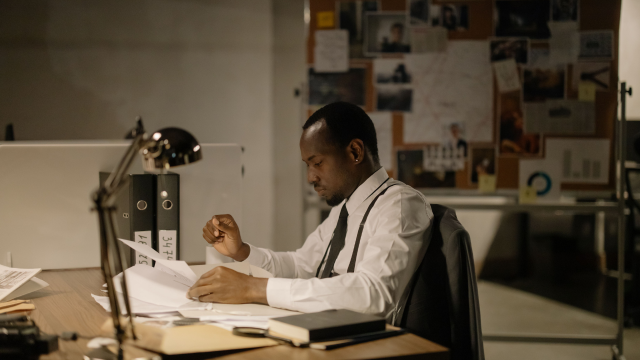 A professional sitting at his desk reviewing paperwork, appearing focused and composed while managing a demanding workload.