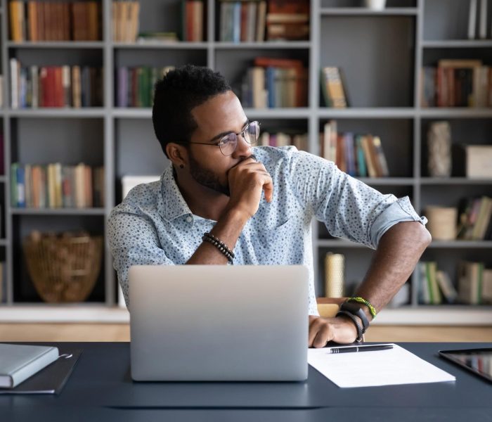 Person sitting at a desk with a laptop, looking thoughtfully out the window in a home office, reflecting on work or personal concerns.